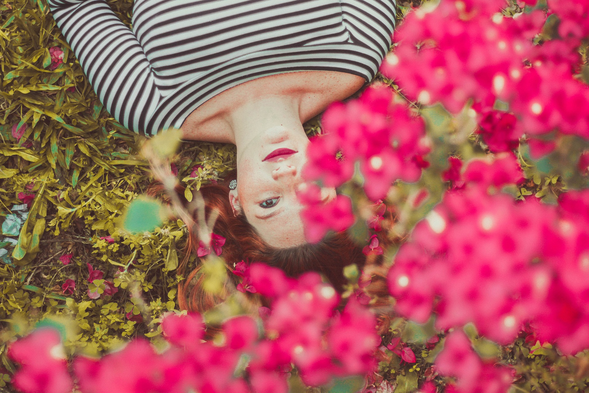 A woman wearing a black and white striped shirt lies under flowers. 