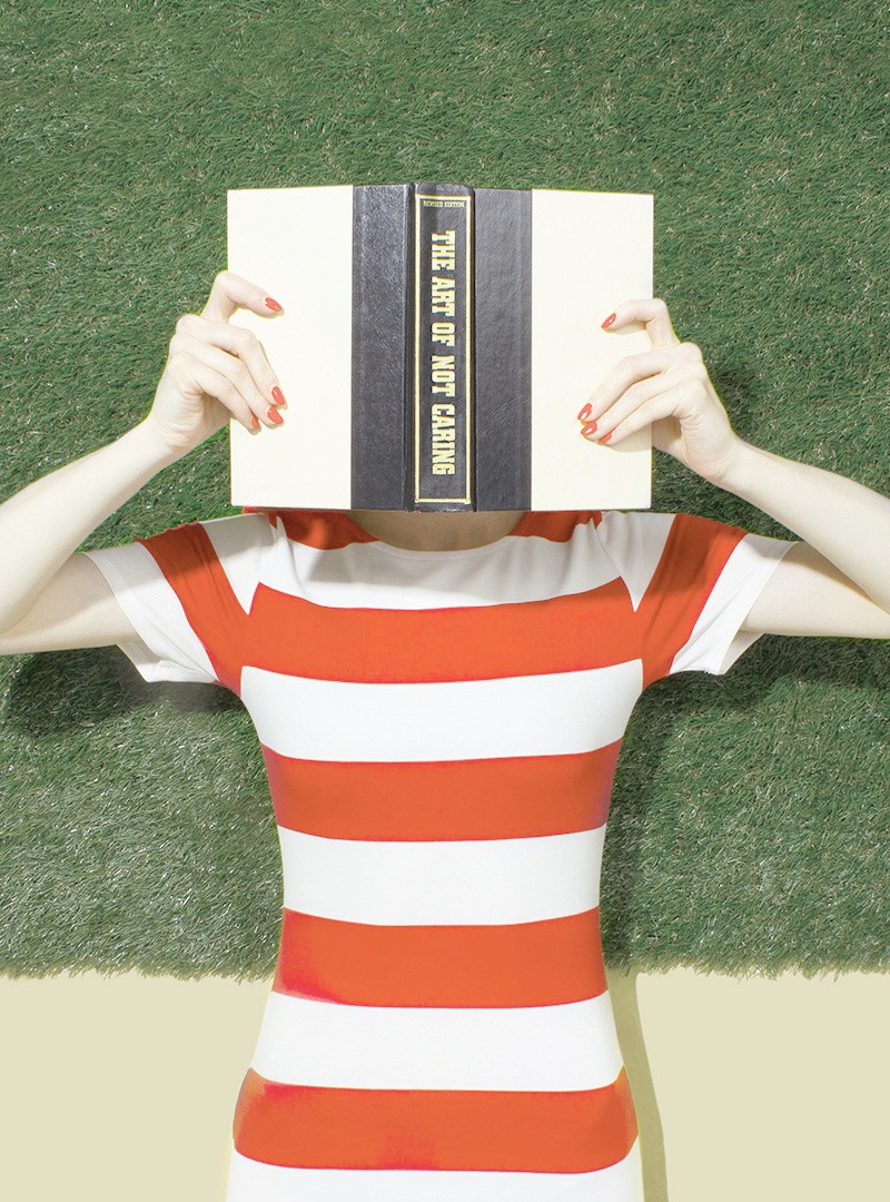 A woman in a red and white striped shirt holding a book above her face. 