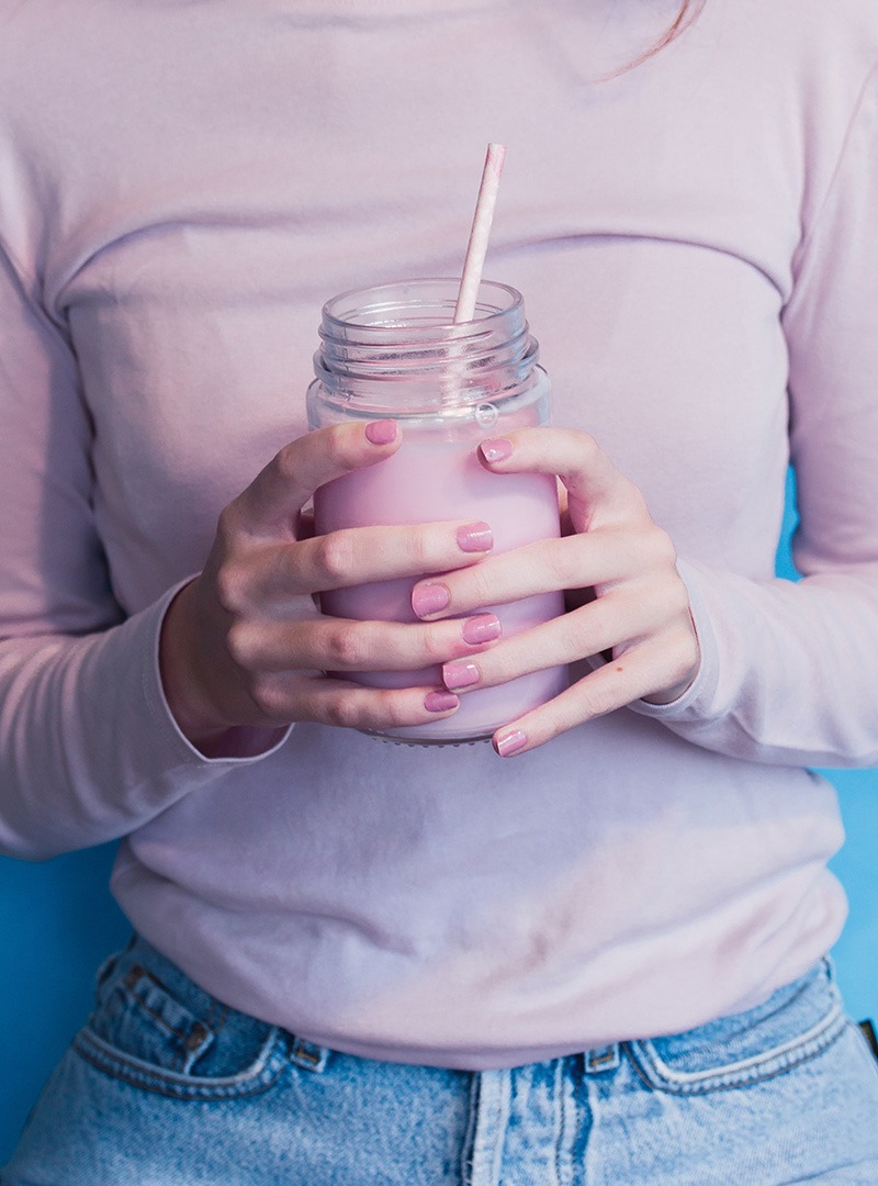 Woman holding a pink drink in a jar, wearing a pink shirt, and having her nails polished in pink color.