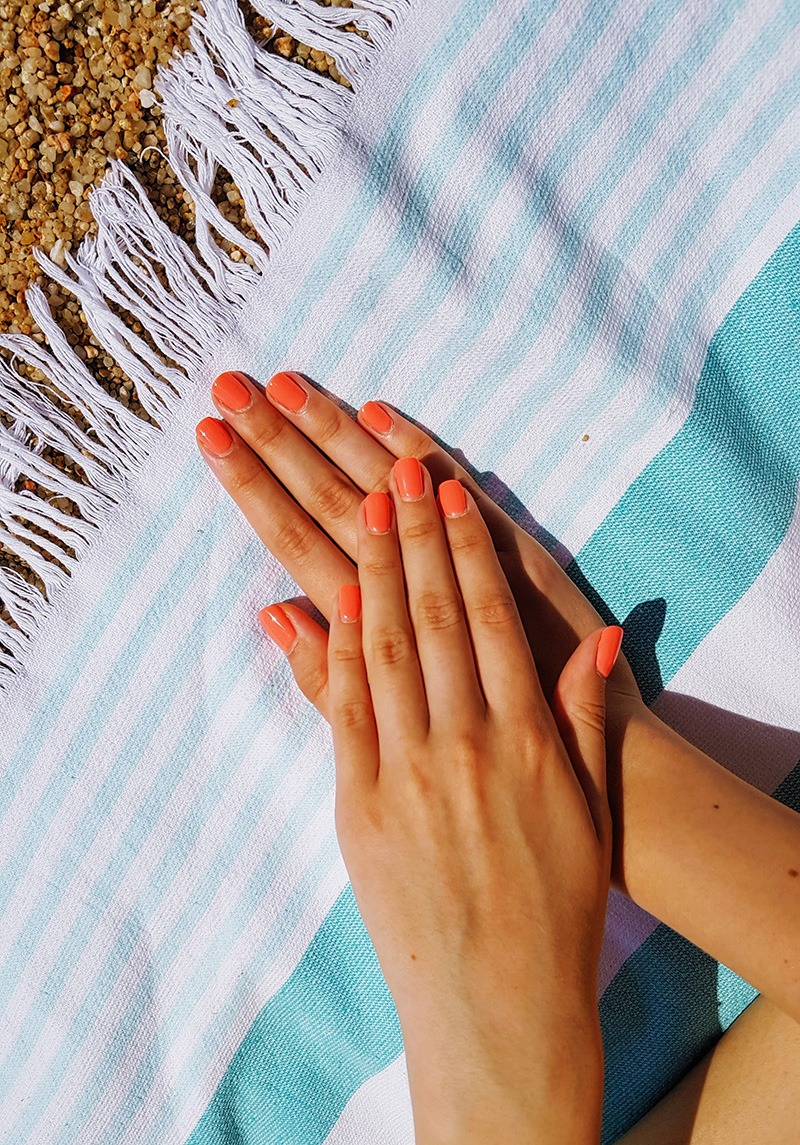 woman's hands with polished nails in coral color on a beach towel